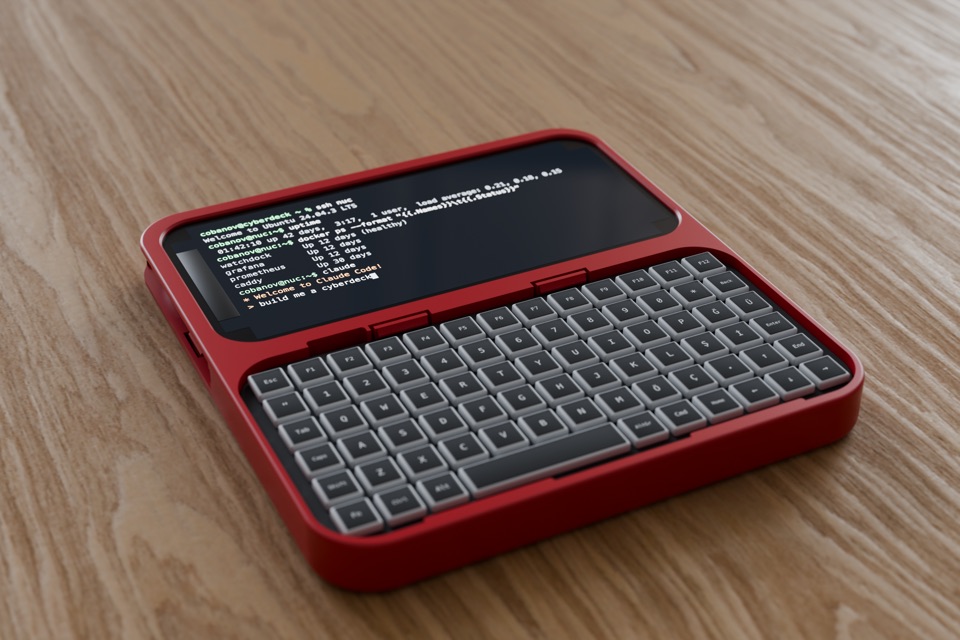 A flat red one-piece slate on a wooden table, holding an iPhone above a compact keyboard, with a terminal on the screen.